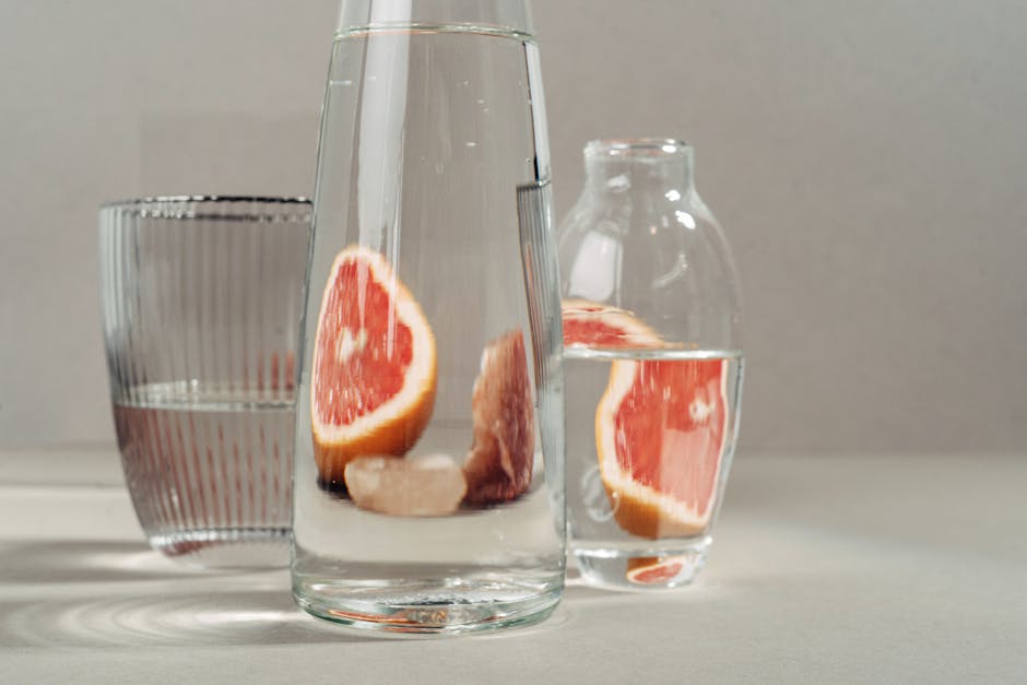 Modern still life of grapefruit slices in water-filled glass bottles on neutral background.